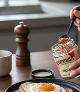 Person adding spice to an egg on toast with a jar of seasoning in a kitchen setting.
