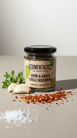 Jar of 'Fermentalists' Herb & Garlic Chilli Seasoning with ingredients on a neutral background